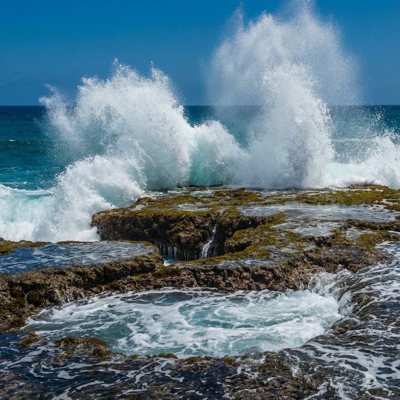 Powerful ocean waves crashing against jagged limestone cliffs at Little Bay